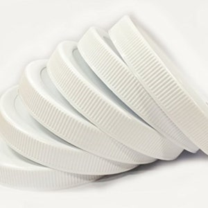 May include: Five white plastic lids with a ridged edge. The lids are stacked on top of each other.