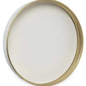 May include: A white plastic lid with a gold metal rim. The lid is round and has a smooth surface.