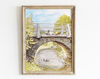 May include: A framed watercolour painting shows a stone bridge over a river, with cartoon characters on the bridge and in the water. The sky is blue with clouds, and trees line the riverbank. The frame has a gold tone. A charming piece of art.