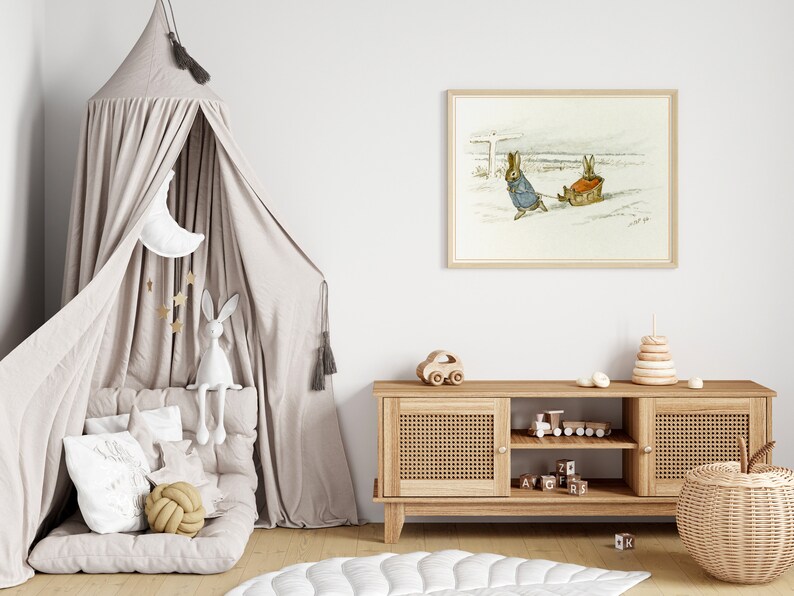 May include: A light brown wooden media console with two doors and two shelves. The console has a woven rattan front and is decorated with a wooden toy car, a wooden train, and a stack of wooden blocks. A white and beige children's play tent is in the background, along with a framed print of two rabbits pulling a sled.