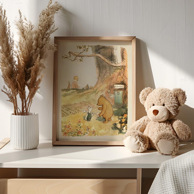 May include: A framed illustration of Winnie the Pooh and Piglet walking in a forest. The illustration is in a light brown frame and is sitting on a white shelf. A brown teddy bear is sitting on the shelf to the right of the frame.