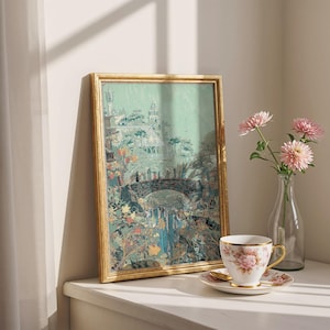 May include: A framed print with a gold-colored frame depicts a landscape with a bridge, waterfall, and buildings. A teacup and saucer with a floral design sit on a white surface, next to a vase with pink flowers.