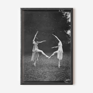 Puede incluir: Fotografía en blanco y negro de dos bailarinas en movimiento, enmarcada en negro. Llevan vestidos fluidos y parecen tocarse los pies. El fondo es una escena exterior borrosa, que sugiere un jardín.