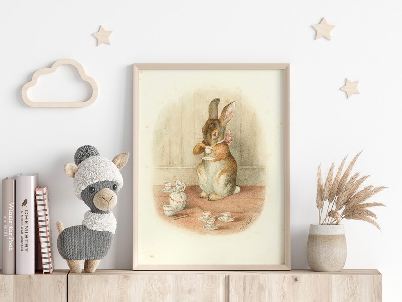 May include: A framed illustration of a brown rabbit holding a teacup, surrounded by a set of miniature teacups and saucers on a table. The rabbit is wearing a pink bow.