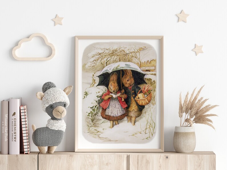 May include: A vintage illustration of two rabbits walking in the snow under an umbrella. The rabbit on the left is wearing a red coat and holding a book. The rabbit on the right is wearing a blue coat and carrying a basket. The illustration is framed in a light wood frame.