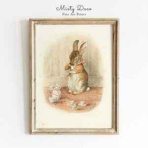 May include: A vintage illustration of a brown rabbit holding a teacup, surrounded by a collection of miniature teacups and saucers on a pink and brown surface. The image is framed in a light wood frame.