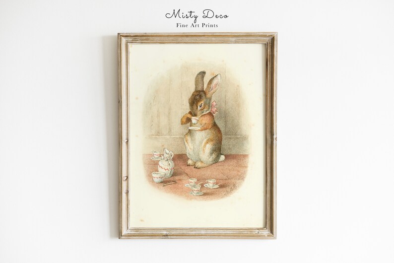 May include: A vintage illustration of a brown rabbit holding a teacup, surrounded by a collection of miniature teacups and saucers on a pink and brown surface. The image is framed in a light wood frame.