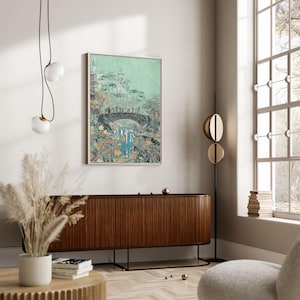 May include: A framed art print depicting a fantasy landscape with a bridge, waterfall, and figures. The artwork features a muted color palette with shades of green, blue, and brown. The print is displayed on a white wall above a wooden cabinet.