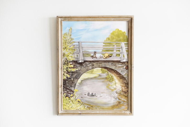 May include: A framed illustration of a stone bridge with a white wooden railing. Two small animals are sitting on the railing, looking at each other. The bridge is over a stream with green trees and a blue sky in the background.
