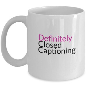 May include: White ceramic coffee mug with the text "Definitely Closed Captioning" in black and pink lettering.