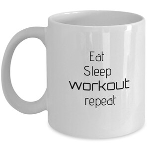 May include: White ceramic coffee mug with black text that reads "Eat Sleep workout repeat".