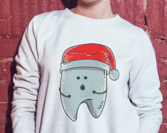 May include: A white sweatshirt with a gray tooth wearing a red Santa hat. The tooth has a surprised expression and is wearing a red Santa hat.