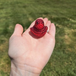 Könnte beinhalten: Eine rote Gummiente, die mit roten, glitzernden Strasssteinen bedeckt ist. Die Ente hat einen roten Schnabel und ein rotes Gesicht.