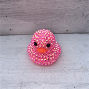 May include: A pink rubber ducky covered in iridescent rhinestones.