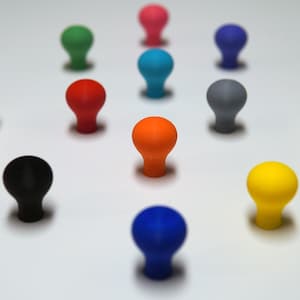 Puede incluir: Surtido de pomos redondos de colores y blancos con un acabado liso y brillante. Los pomos están dispuestos en un patrón circular sobre una superficie blanca.