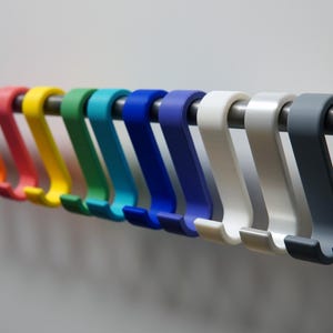 May include: A row of colorful S-shaped hooks in a variety of colors, including red, orange, yellow, green, blue, white, gray, and black. The hooks are hanging on a silver metal rod.