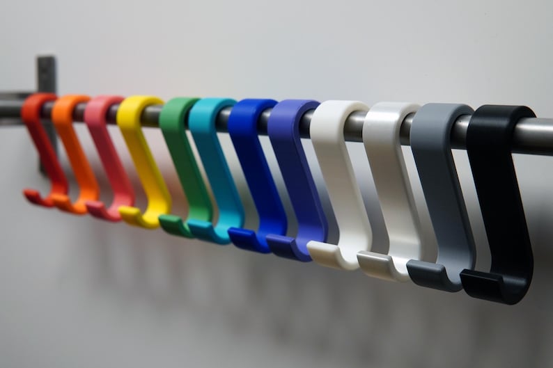 May include: A row of colorful S-shaped hooks in a variety of colors, including red, orange, yellow, green, blue, white, gray, and black. The hooks are hanging on a silver metal rod.