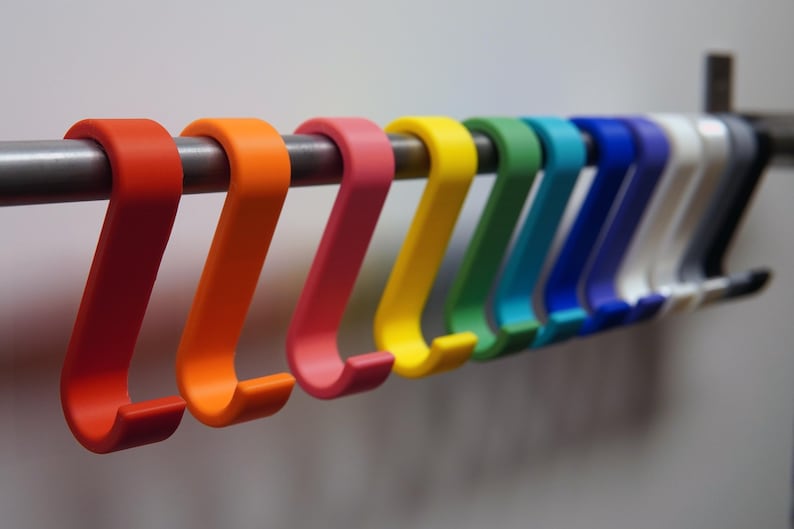 May include: A row of colorful S-shaped hooks in red, orange, pink, yellow, green, teal, blue, white, and gray. The hooks are hanging on a silver metal rod. The hooks are made of a smooth, matte material.