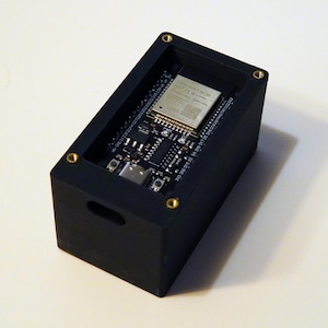 Könnte beinhalten: Ein schwarzes Plastikgehäuse mit goldenen Schrauben, das eine kleine Platine mit einem Chip und anderen Komponenten enthält.
