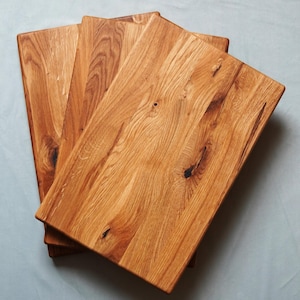 Pode incluir: Um conjunto de quatro tábuas de corte retangulares de madeira clara, empilhadas. A madeira apresenta veios e nós visíveis. As tábuas estão ligeiramente sobrepostas, revelando a textura natural da madeira. Cada tábua mede cerca de 30 cm.