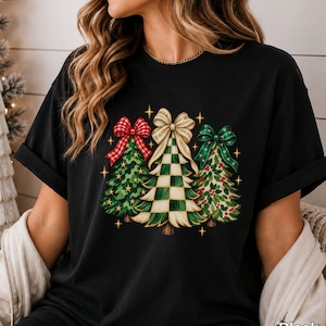 May include: A black t-shirt featuring a graphic of three stylised Christmas trees. The left tree has a red plaid bow, the centre tree has a cream and green chequered pattern with a cream bow, and the right tree has a green bow.