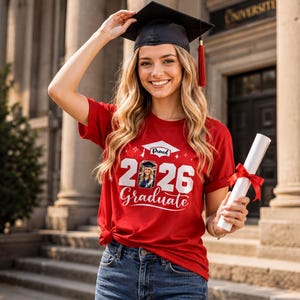 A smiling young woman wearing a graduation cap and gown, holding a diploma, standing in front of a university building.