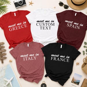 a collection of t-shirts with custom text printed on them, arranged on a table with various travel-related items such as sunglasses, a hat, and a compass.