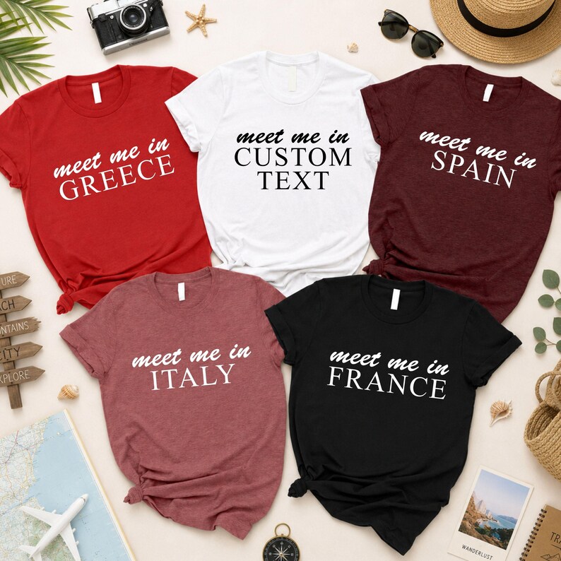a collection of t-shirts with custom text printed on them, arranged on a table with various travel-related items such as sunglasses, a hat, and a compass.