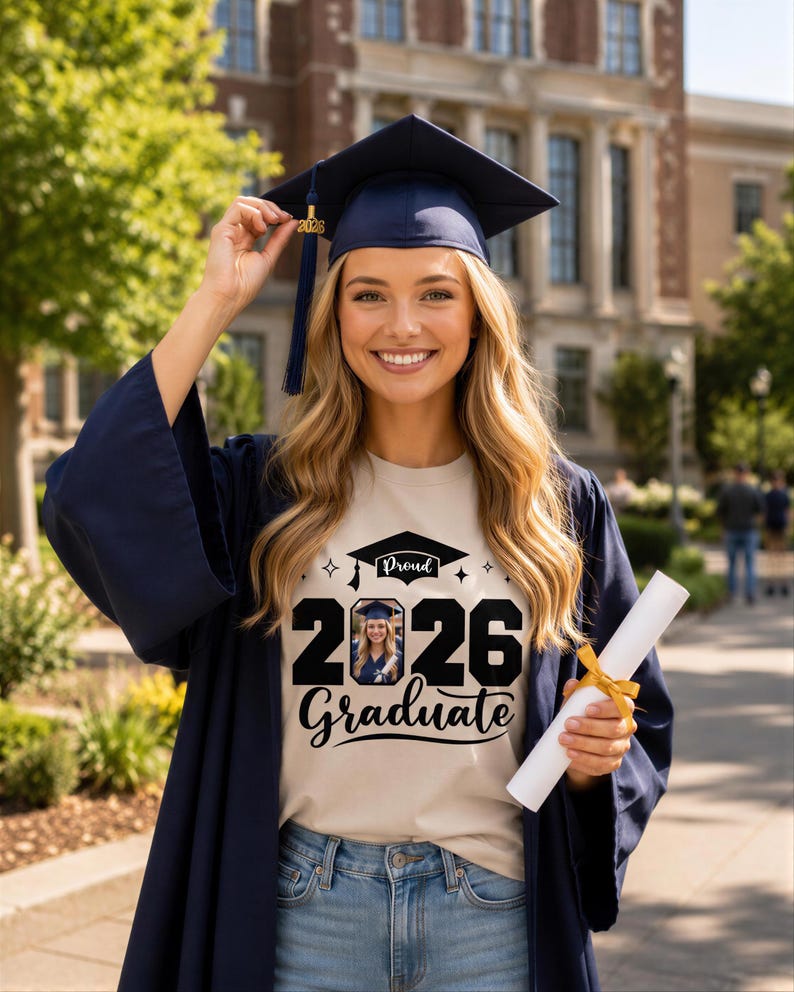 A smiling young woman in a graduation gown and cap holding a diploma stands in front of a brick building.