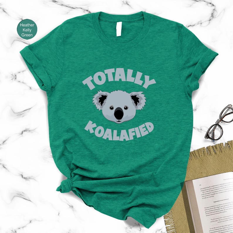 A green t-shirt with a cartoon koala and the text "Totally Koalified" printed on it, along with a pair of glasses and a book.