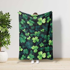May include: A dark green blanket featuring a pattern of various sized green shamrocks. The shamrocks are in shades of light and dark green, creating a layered effect. The background is a dark, almost black color.