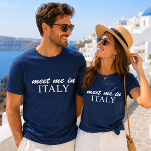 A man and a woman wearing matching blue t-shirts with the text "Meet me in ITALY" are standing together and smiling.
