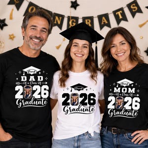 Three people wearing graduation t-shirts stand together, smiling, with a graduation banner and balloons in the background.