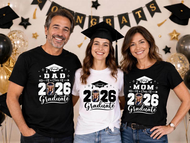 Three people wearing graduation t-shirts stand together, smiling, with a graduation banner and balloons in the background.