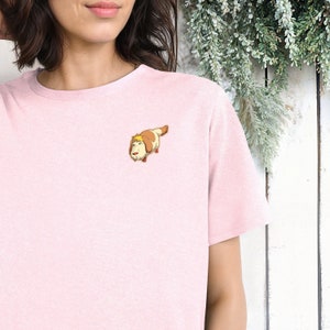 May include: A pink t-shirt with a cartoon dog illustration on the front. The dog is brown and white with a yellow head and is looking to the left.