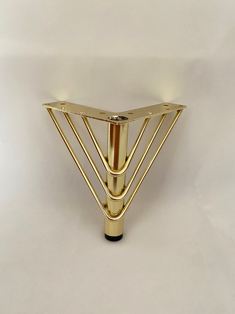 May include: Gold metal furniture leg with a triangular base and four horizontal bars. The leg has a black plastic foot.