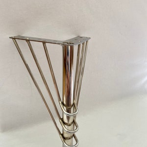 May include: A silver metal furniture leg with a square base and four curved supports. The leg is designed to be attached to a piece of furniture.