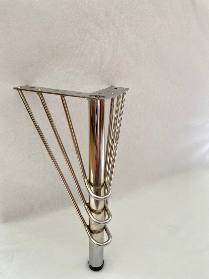 May include: A silver metal furniture leg with a square base and four curved supports. The leg is designed to be attached to a piece of furniture.