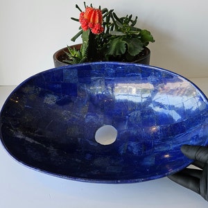 May include: A large, oval-shaped sink made of blue lapis lazuli stone. The sink has a smooth, polished surface and a small drain hole in the center.