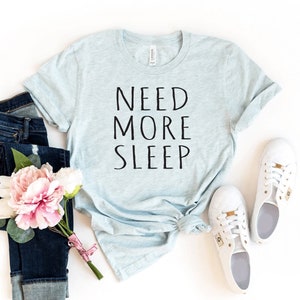 May include: A light blue t-shirt with the text "NEED MORE SLEEP" printed in black.