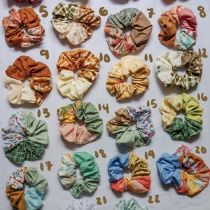 May include: Twenty-two colorful scrunchies made from different patterned fabrics. The scrunchies are arranged in rows on a white surface.