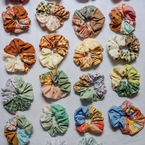 Pode incluir: Uma coleção de 20 scrunchies de tecido coloridos com vários padrões. Os scrunchies são feitos de diferentes tecidos, incluindo flores, xadrez e bolinhas.