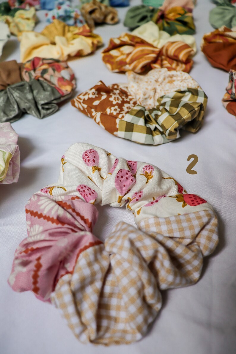 May include: A set of colorful fabric scrunchies with various patterns, including floral, gingham, and strawberry prints. The scrunchies are made of soft, stretchy fabric and are perfect for holding hair in place.
