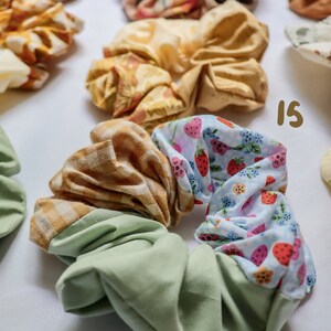 May include: A green, yellow, and blue patterned scrunchie with a strawberry print. The scrunchie is made of fabric and is a popular hair accessory.
