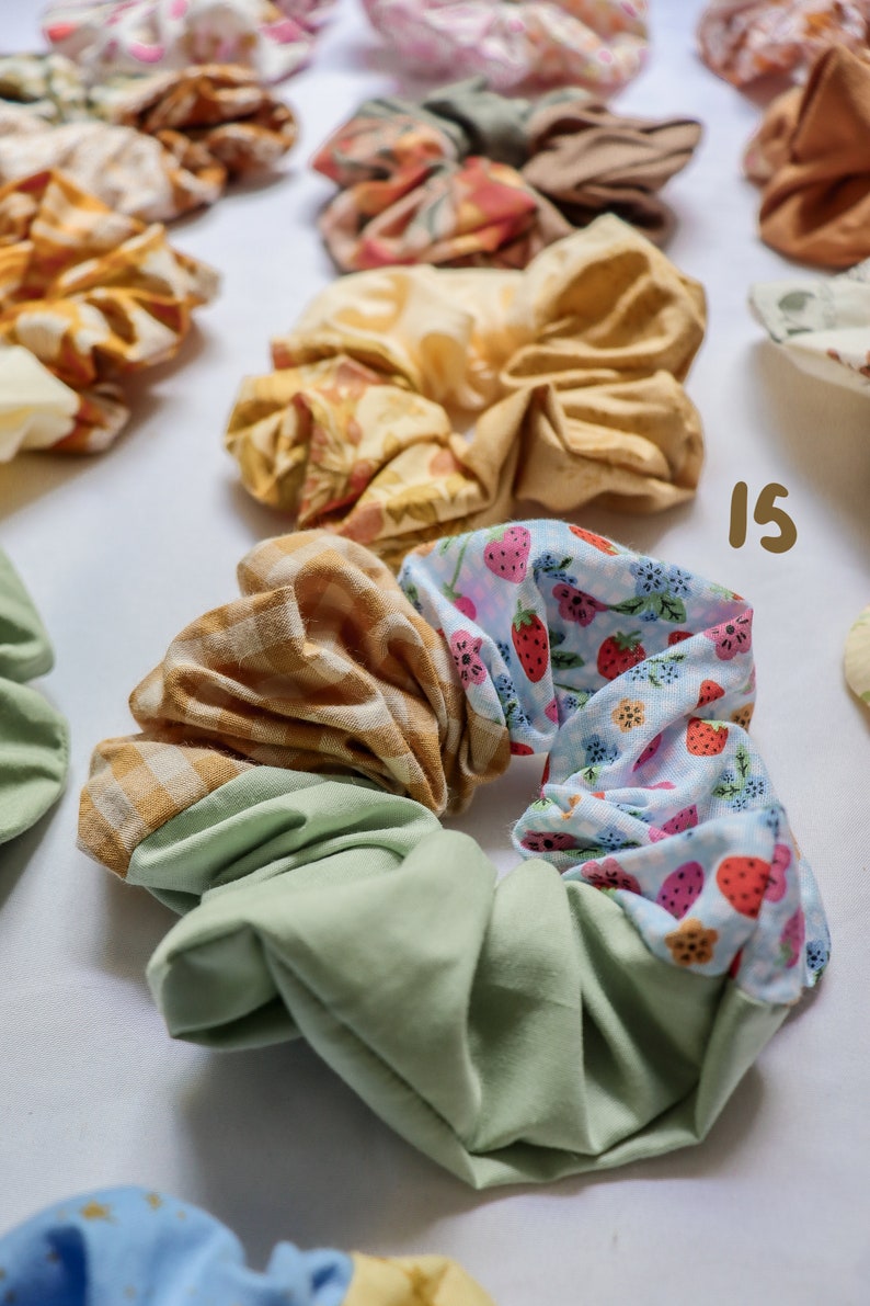 May include: A green, yellow, and blue patterned scrunchie with a strawberry print. The scrunchie is made of fabric and is a popular hair accessory.