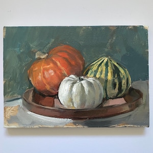 May include: An oil painting on canvas depicting a still life of three gourds on a round brown tray. The arrangement includes one large orange pumpkin, one smaller white pumpkin, and one green and yellow striped gourd against a dark green background.