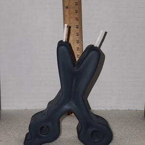 May include: A dark gray, candle shaped like a pair of scissors with white wicks.