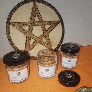 Peut inclure: Trois bocaux en verre avec des couvercles noirs et des breloques argentées. Chaque bocal contient une poudre brune et porte une étiquette blanche sur laquelle est inscrit "Magic Energy 11 VOLADORA POWDER".