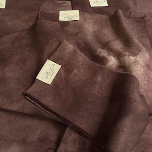 May include: Close-up of several pieces of fabric in varying sizes, all in a deep burgundy color. Each piece has a tag that reads "Stella Wool" in elegant script. The fabric appears soft and textured.