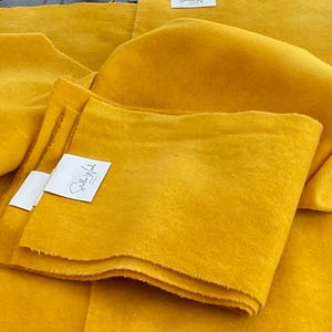 May include: Several pieces of bright yellow fabric are arranged in a layered composition. Some pieces are folded, and others are spread out, showcasing the texture and color. Small white tags are attached to some pieces.